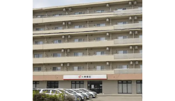 正面に駐車場がある、ベージュ系タイル張りの7階建てマンション。1階にはテナントが入居