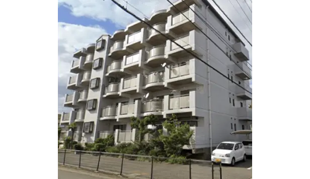 白いタイル外壁と曲線のバルコニーが特徴的な中層マンション。敷地には植栽と駐車場あり