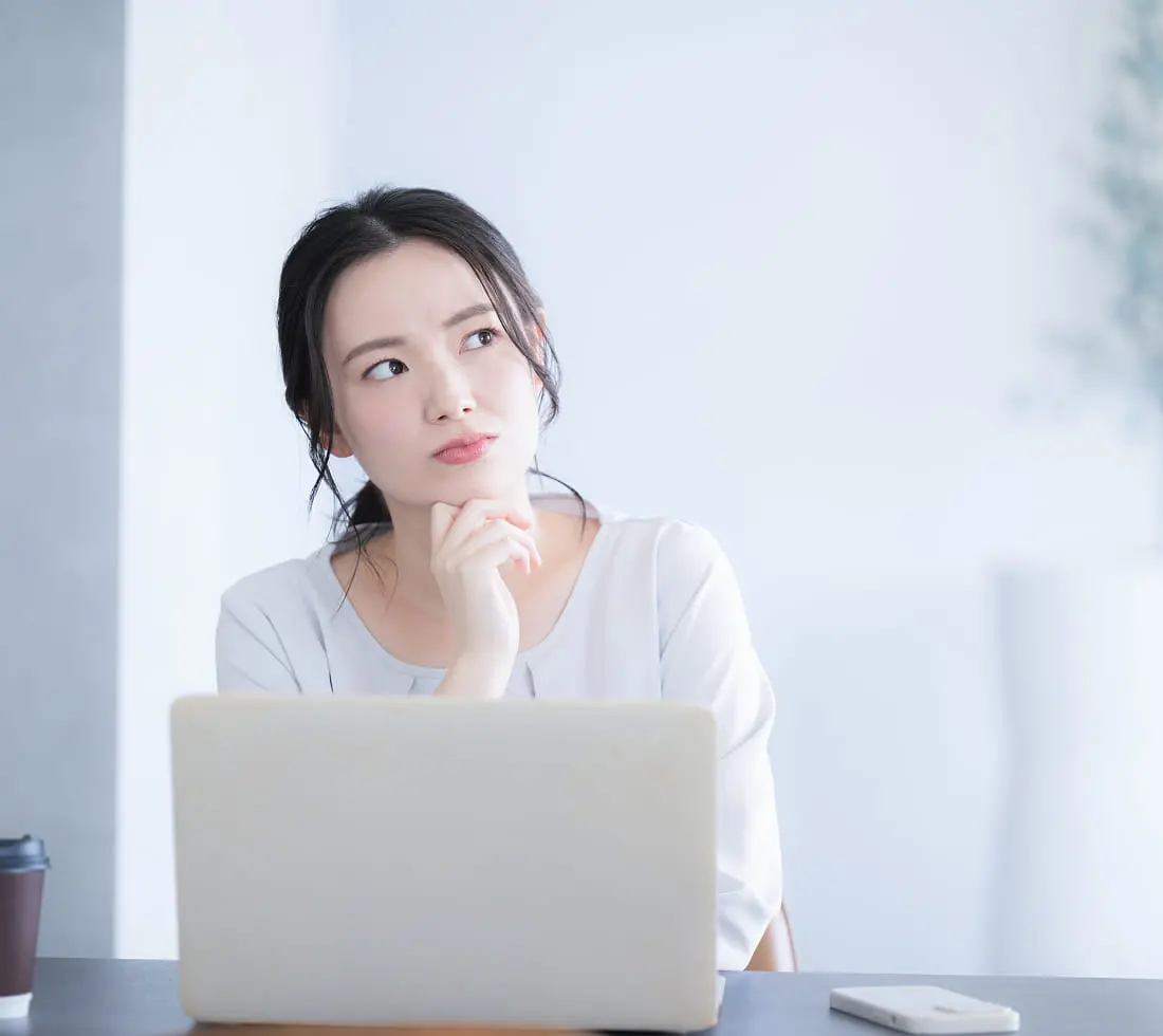 ノートパソコンの前で考え込む表情の若い女性