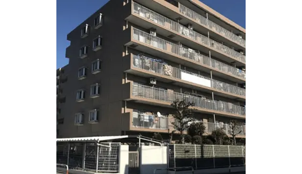 複数階建ての茶色い外観のマンション。バルコニーが特徴的で、木々が並ぶ落ち着いた住宅街に立地。